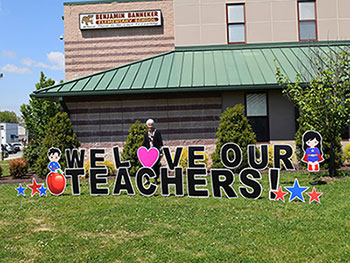 Teacher standing outside school with sign saying We Love Our Teachers.
